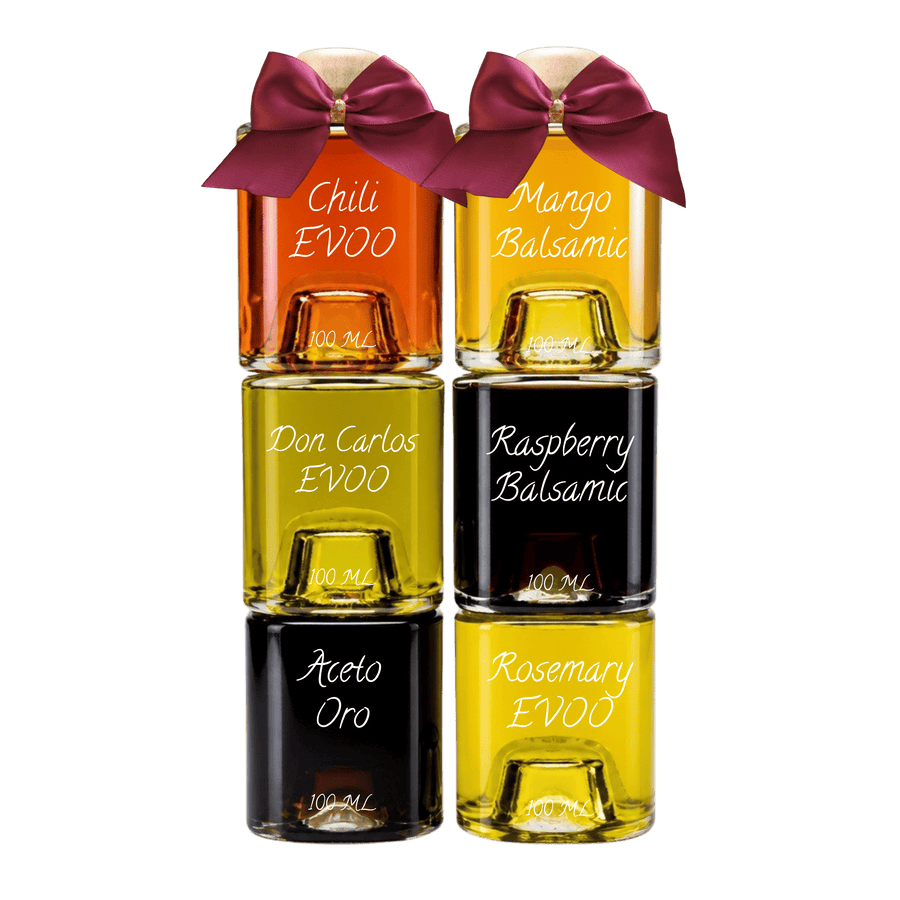 Six small glass bottles of EVOO balsams and oils arranged in a 2x3 grid on a white background. Each bottle has a dark bow on top and is labeled with the scent or type name in white script: Chili, Mango Balsamic, Don Carlos EVOO, Raspberry Balsamic, Aceto Oro, and Rosemary EVOO.
