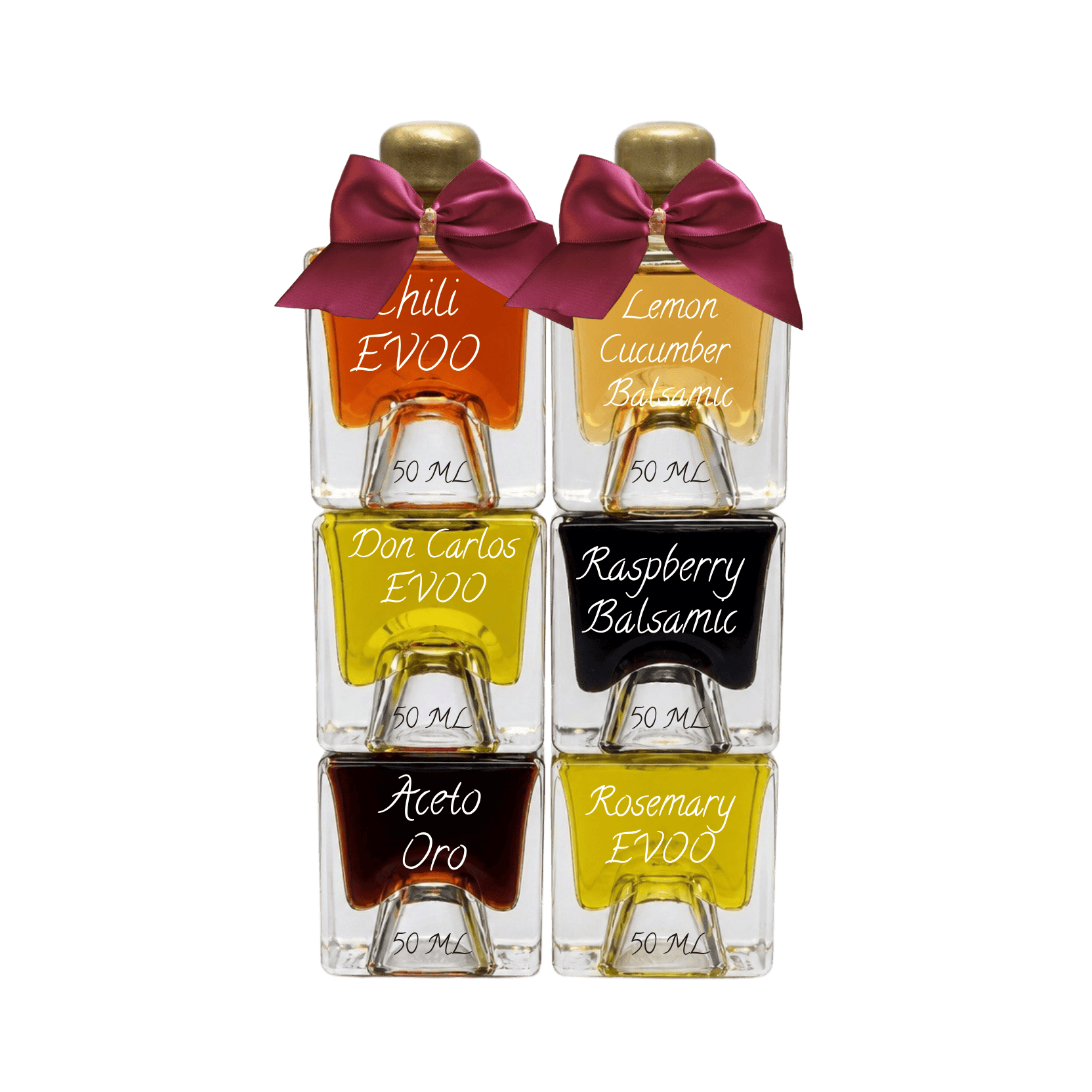 Six small glass bottles of EVOO balsams and accents arranged in a 2x3 grid on a white background. The bottles contain orange, yellow, black, and dark brown liquids, are topped with gold caps and purple bows, and feature white script labels reading 'Chili EVOO', 'Lemon Cucumber Balsamic', 'Don Carlos EVOO', 'Raspberry Balsamic', 'Aceto Oro', and 'Rosemary EVOO'.