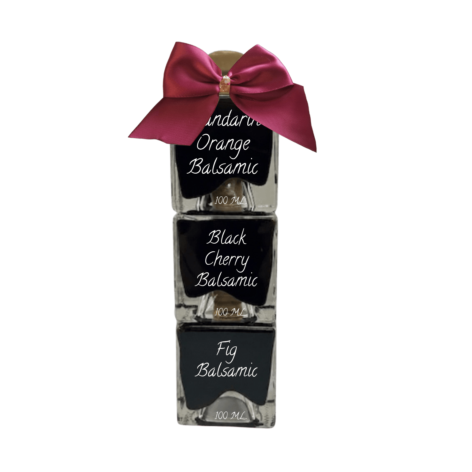 Three stacked glass bottles of balsamic syrup with black labels, tied together with a large magenta satin bow on top, shown against a plain white background.