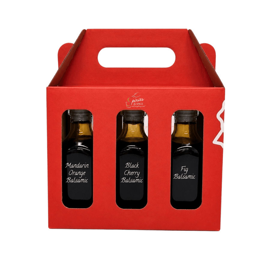 A red cardboard gift box with a handle, containing three small dark glass bottles of balsamic vinegar labeled Mandarin Orange Balsamic, Black Cherry Balsamic, and Fig Balsamic.