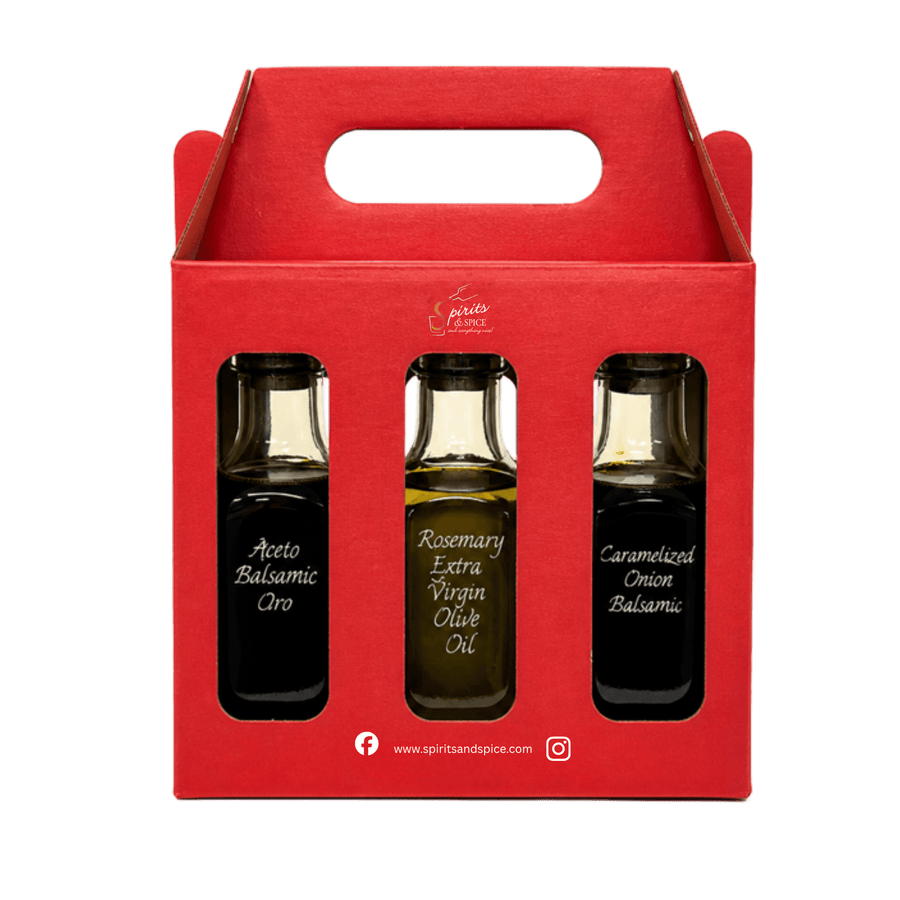 A red cardboard gift box with a handle, holding three glass bottles of olive oil and balsamic. The center bottle is labeled 'Rosemary Extra Virgin Olive Oil', while the side bottles are labeled 'Aceto Balsamico Oro' and 'Caramalized Onion Balsamic'.