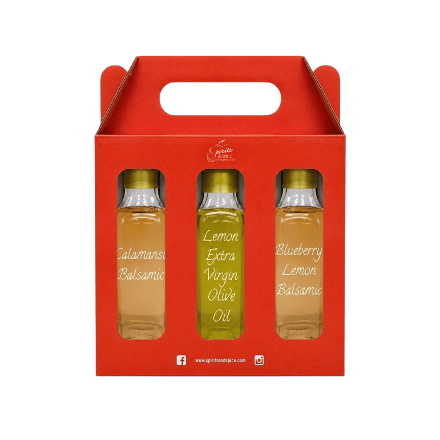 A red gift box with a handle containing three small glass bottles of oil. The center bottle is labeled 'Lemon Extra Virgin Olive Oil' and the side bottles are labeled 'Calamansi Balsamic' and 'Blueberry Lemon Balsamic'.