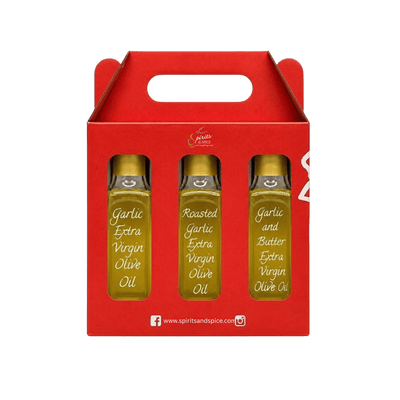 A red gift box with a handle containing three small glass bottles of olive oil, labeled Garlic Extra Virgin Olive Oil, Roasted Garlic Extra Virgin Olive Oil, and Garlic and Butter Extra Virgin Olive Oil, on a white background.